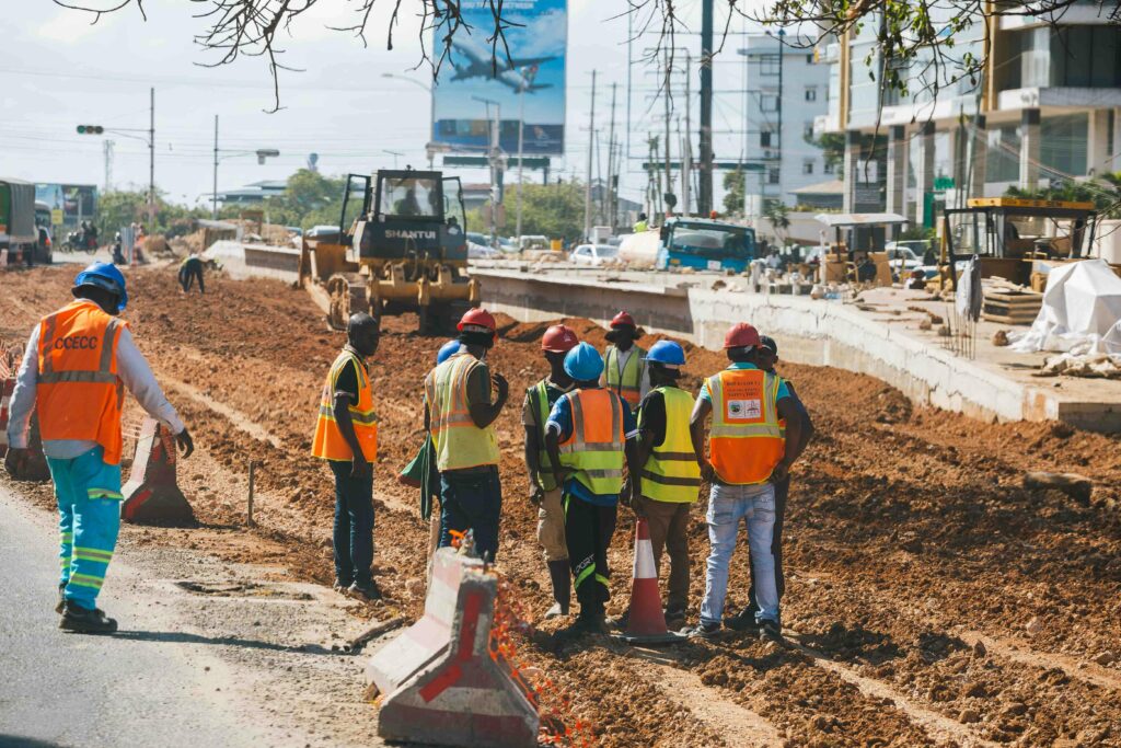 Construction workers wearing safety gear at a busy roadwork site during the day.