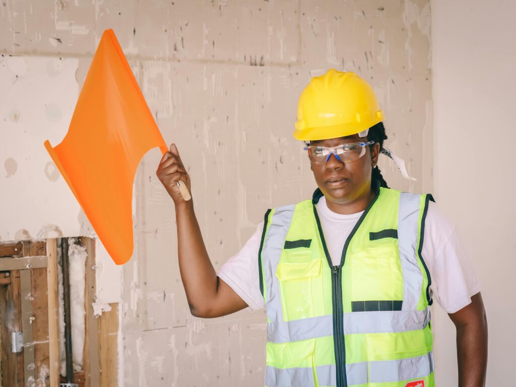 Female construction worker in safety gear with orange flag indoors, showcasing occupational safety.